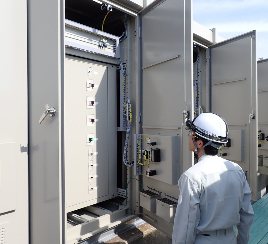 屋外の受変電設備の扉を開けて点検する作業員