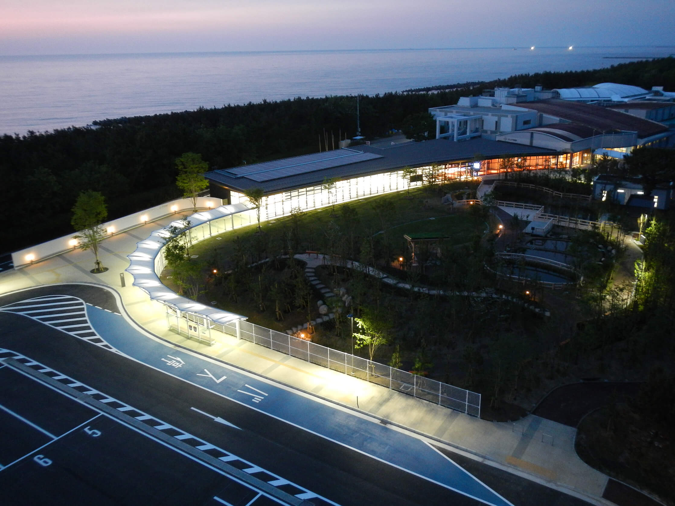 夕暮れの海沿いに灯りがともる施設